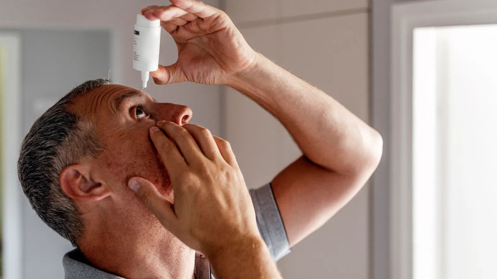 Patient applying lubricant eye drops for dry eye treatment